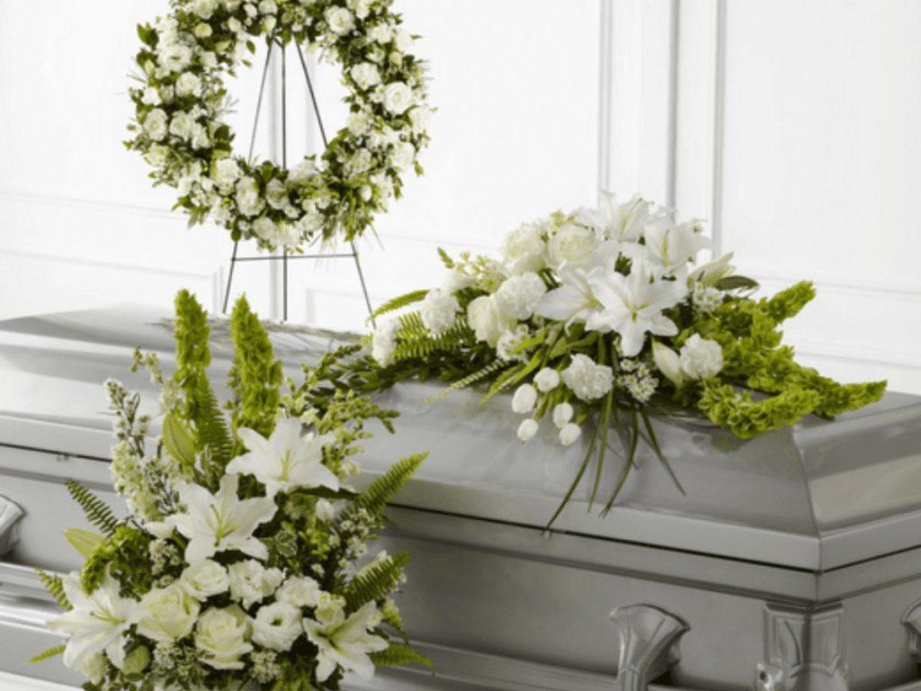 corona funebre blanca y arreglos florales blancos sobre ataud gris